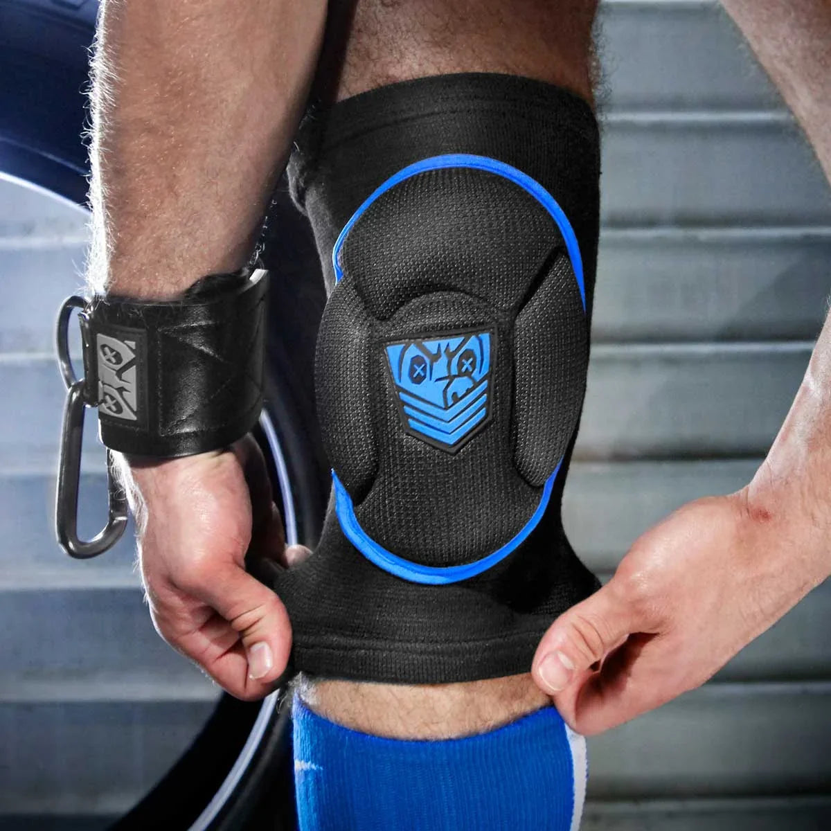 Hands pulling a blue trim Skullfuck knee pad up over the knee, cuffed wrist in frame, Fort Troff gay gear at Boyzshop