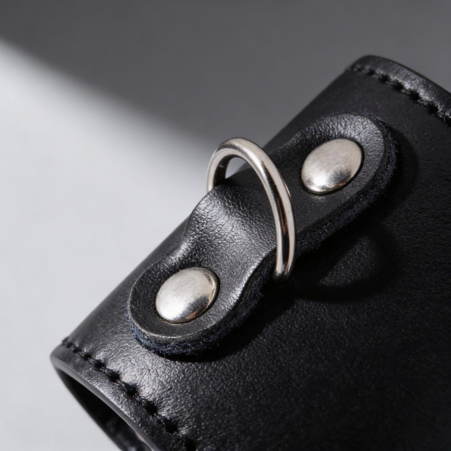 close-up of metal D-ring attachment on black leather ball stretcher with silver rivet hardware
