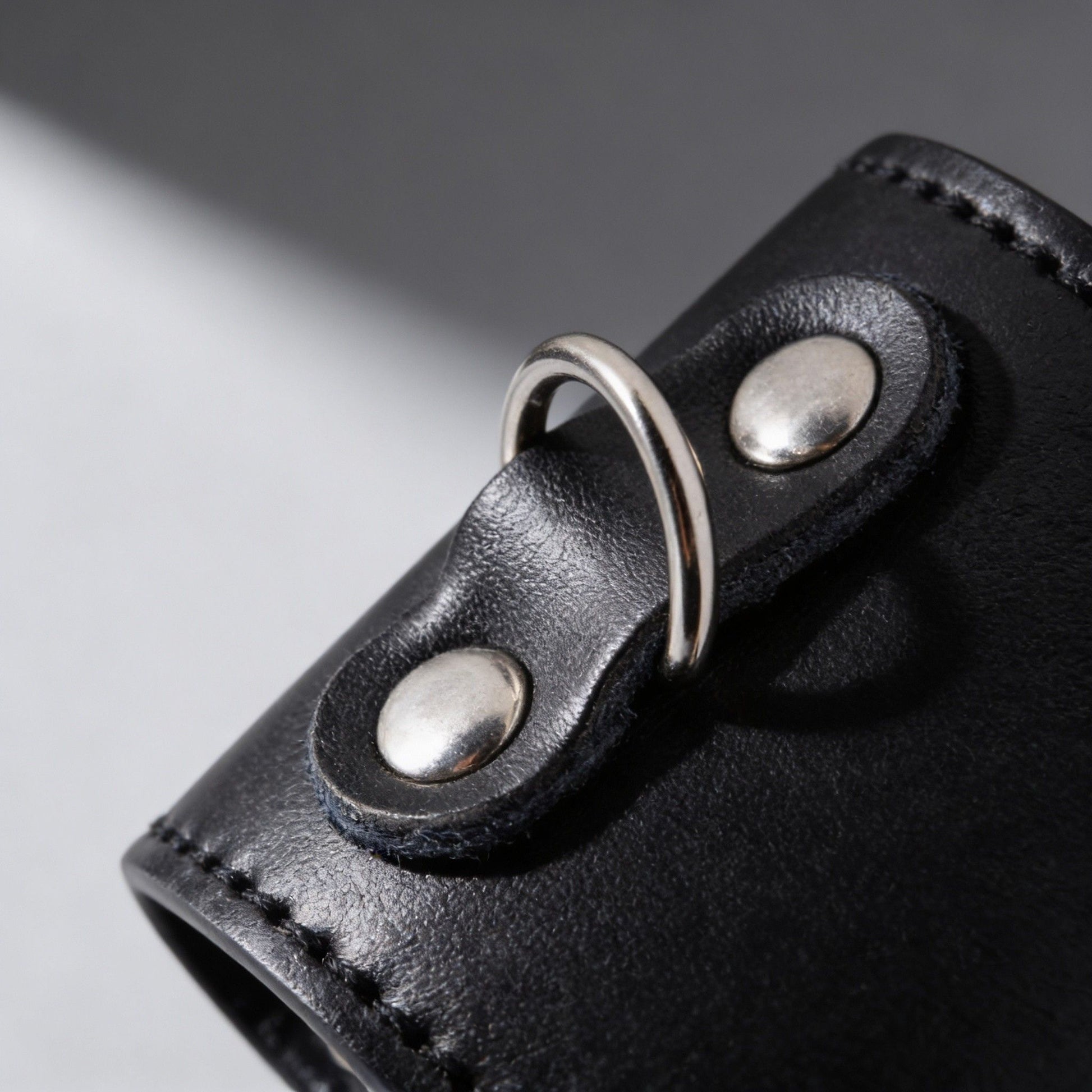 close-up of metal D-ring attachment on black leather ball stretcher with silver rivet hardware