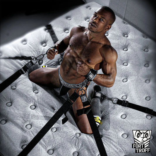 Muscled Black man in a jock spread out on a mattress, wrists tied with bed restraints, Fort Troff gay gear at Boyzshop
