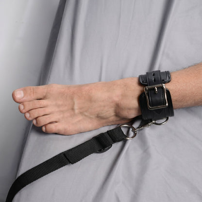 black padded ankle restraint cuff attached to adjustable under-bed restraint strap on gray bedding