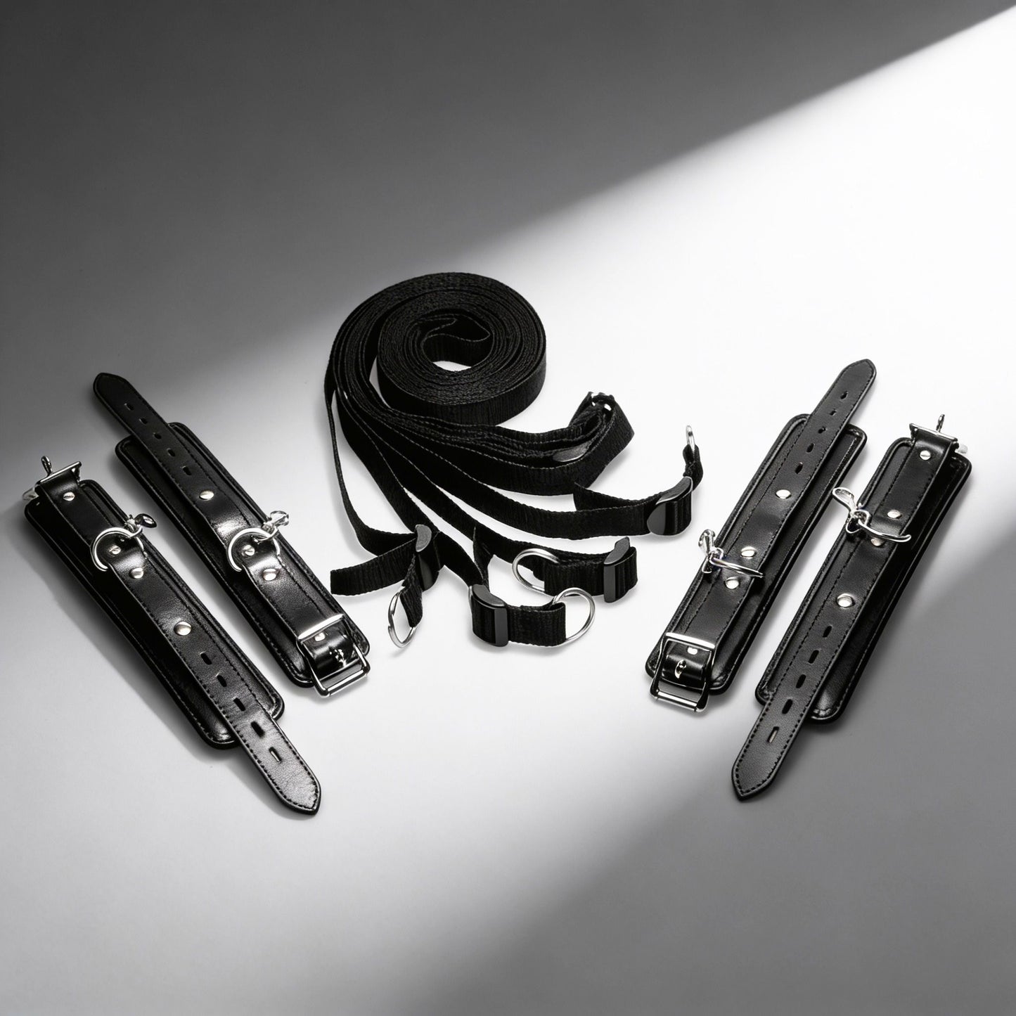 black under-bed restraint kit with adjustable straps, padded cuffs, buckles, and silver clip hardware displayed on white background