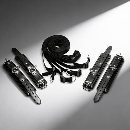 black under-bed restraint kit with adjustable straps, padded cuffs, buckles, and silver clip hardware displayed on white background