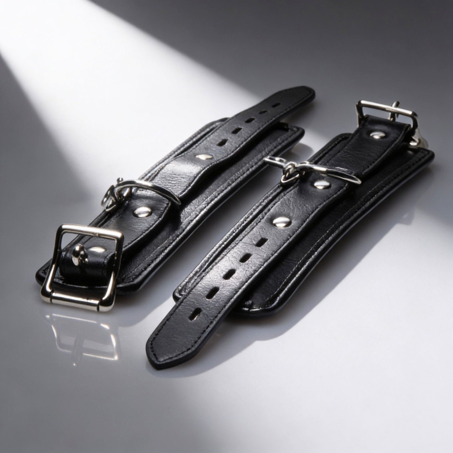 pair of black padded restraint cuffs with adjustable buckle straps and silver hardware detail