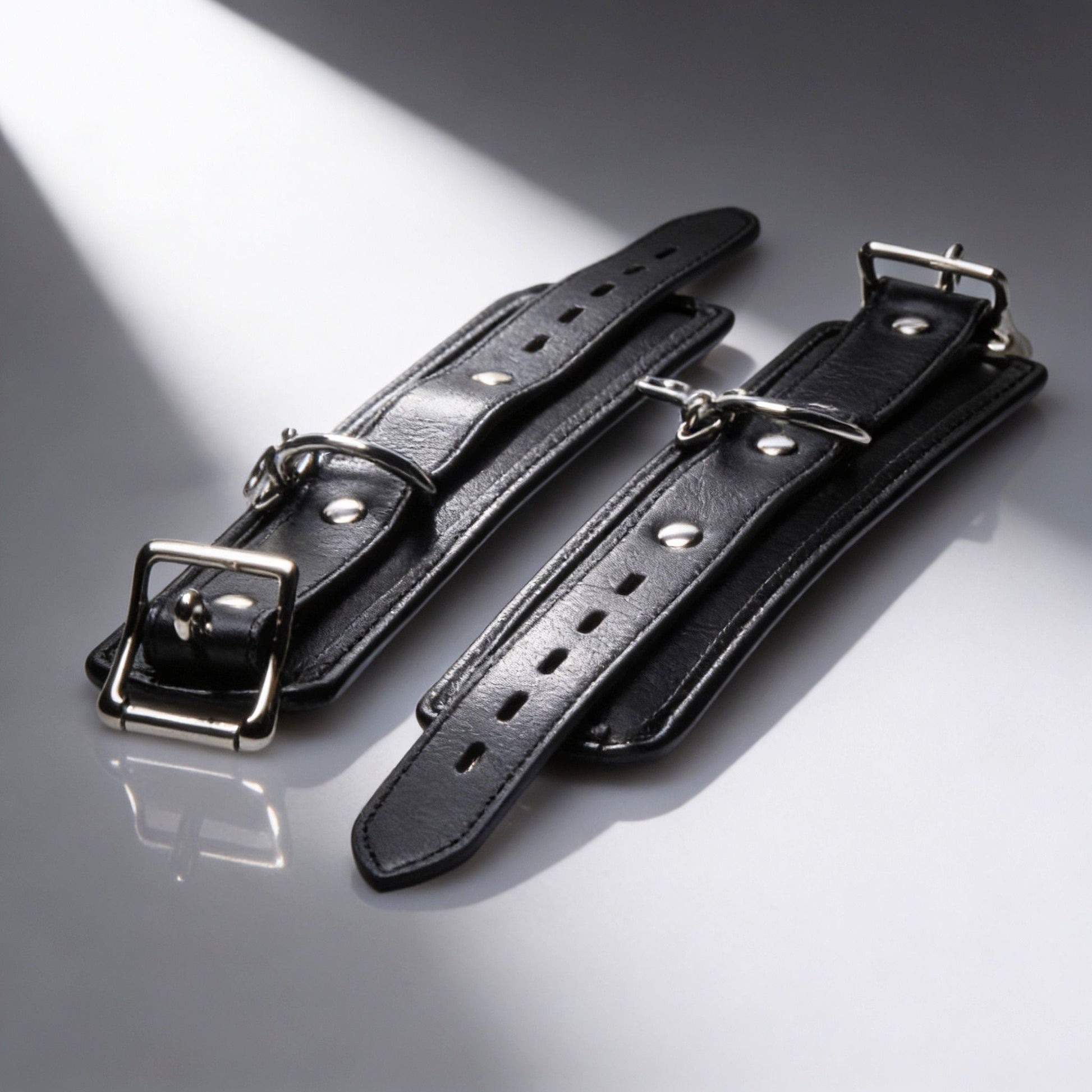 pair of black padded restraint cuffs with adjustable buckle straps and silver hardware detail