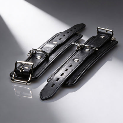 pair of black padded restraint cuffs with adjustable buckle straps and silver hardware detail