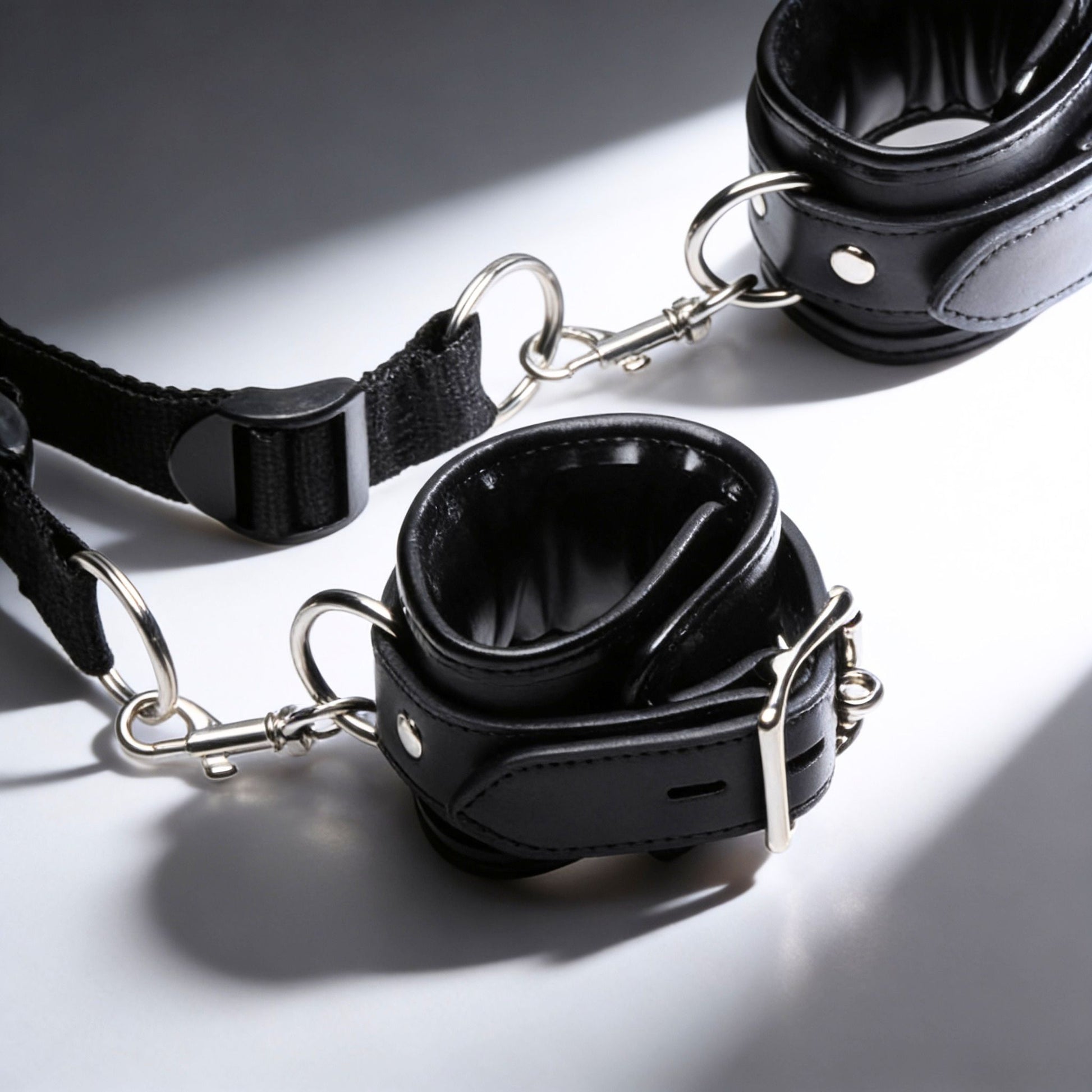 close-up of padded black restraint cuff with silver clip hardware and adjustable nylon strap connection