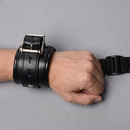 black padded wrist restraint cuff with silver buckle connected to adjustable bed restraint strap