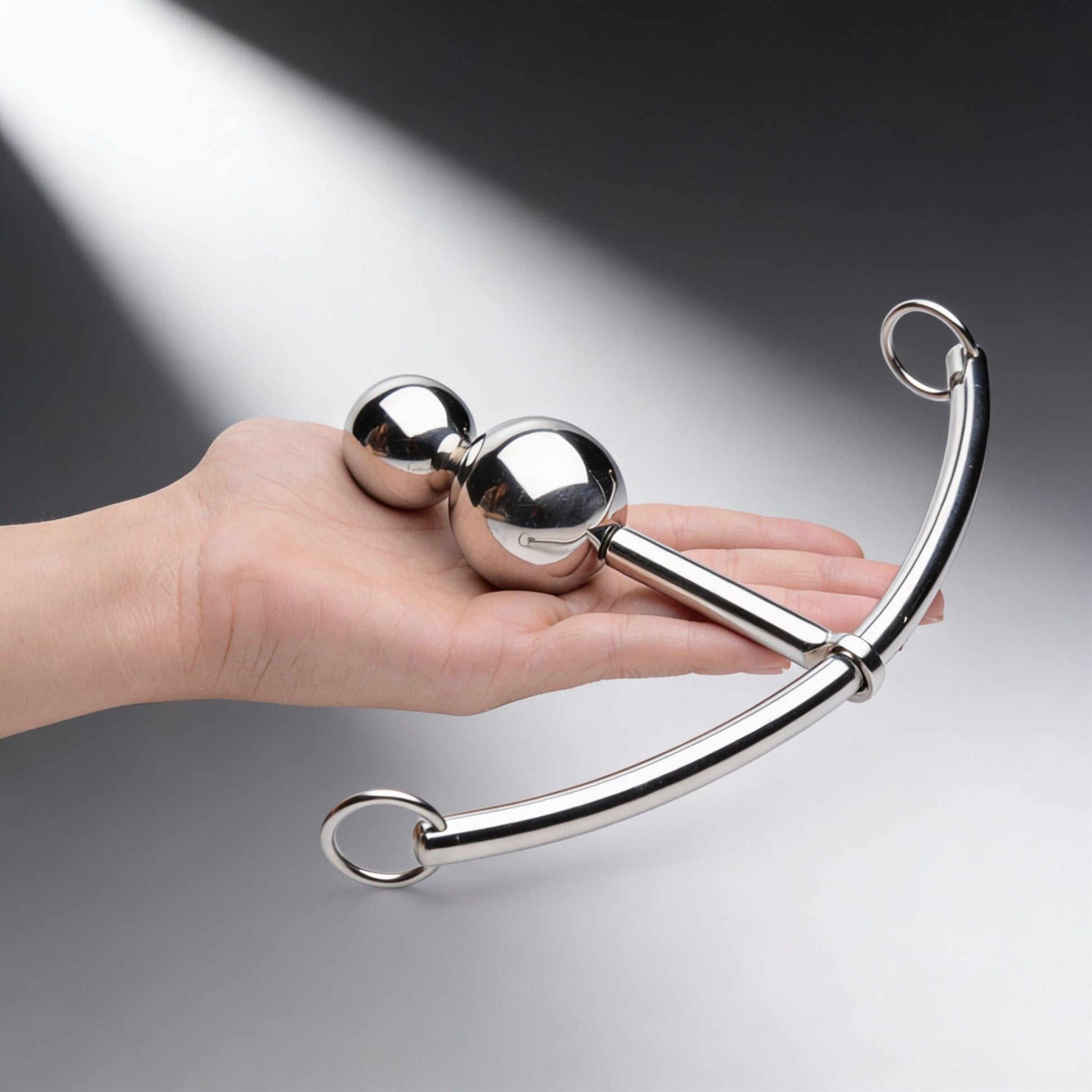hand holding stainless steel double ball plug with curved rod and adjustable sliding O ring attachment on white background