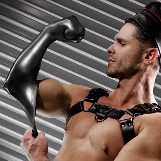 Harnessed model flexing an arm sheathed in the FFister Black fisting sleeve, Fort Troff