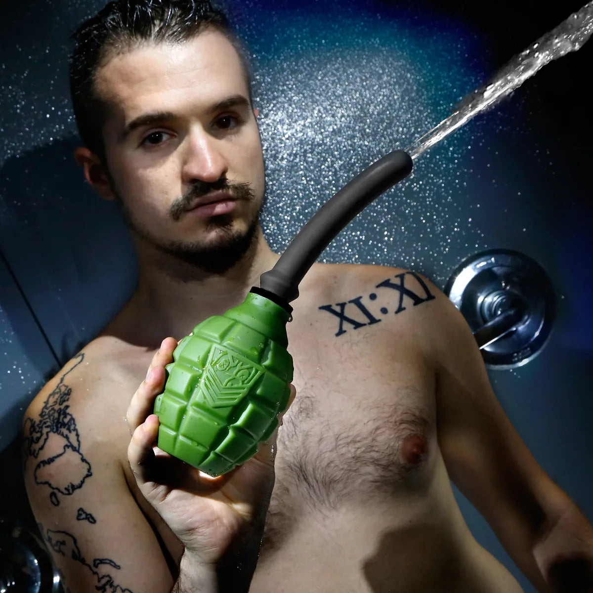 Tattooed model in a shower holding the green Grenade anal douche bulb as water sprays out, Fort Troff gay gear at Boyzshop
