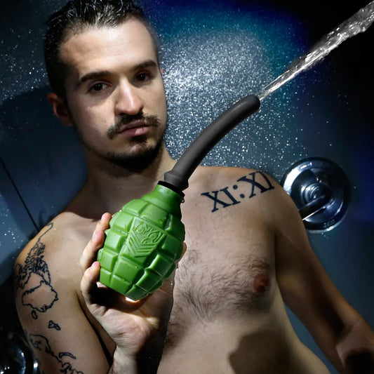 Tattooed model in a shower holding the green Grenade anal douche bulb as water sprays out, Fort Troff gay gear at Boyzshop