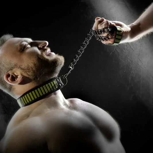 Model on a chain leash pulled tight by a hand, Tactical Velcro collar with olive stripes on his neck, Fort Troff gay gear at Boyzshop