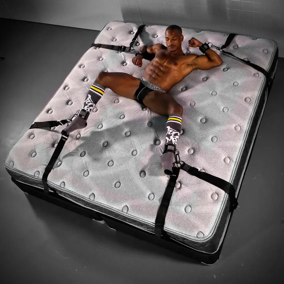 Overhead view of a man strapped spread-eagle with under bed restraints on a big bed, Fort Troff gay gear at Boyzshop