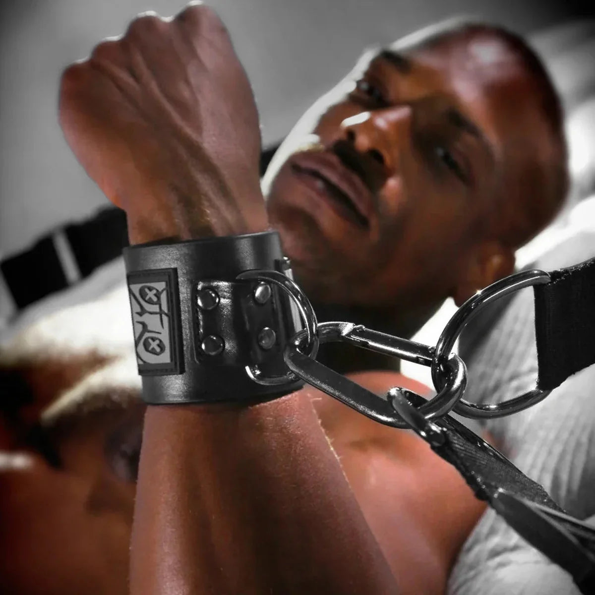 Close-up of a leather wrist cuff clipped to a bed restraint strap with a steel clip, Fort Troff gay gear at Boyzshop