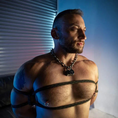 Model in a chain collar looking away, chest harness tied in olive Grunt bondage rope, Fort Troff gay gear at Boyzshop