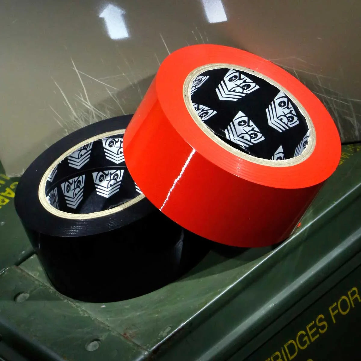 Red Mega-Roll bondage tape roll beside a black roll on an olive ammo box, shield print inside, Fort Troff gay gear at Boyzshop