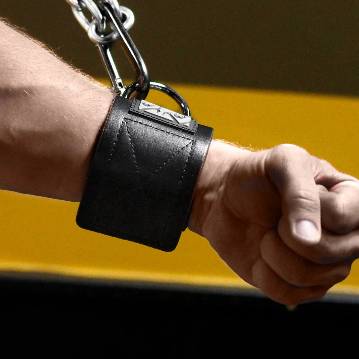Black Neo neoprene wrist cuff on a clenched fist, steel D-ring hooked to a chain, Fort Troff gay gear at Boyzshop