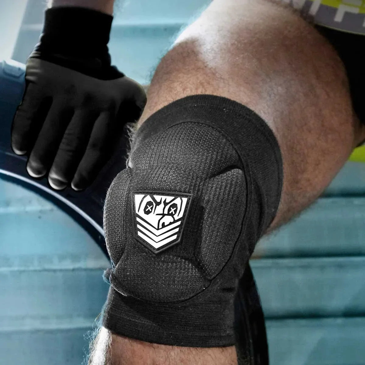 Black Skullfuck knee pad strapped over a knee, white Fort Troff shield on the thick cushion, Fort Troff gay gear at Boyzshop