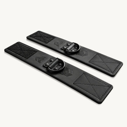 Leather ankle cuffs pair laid flat on white, stitched Velcro panels with dark D-rings, Fort Troff gay gear at Boyzshop