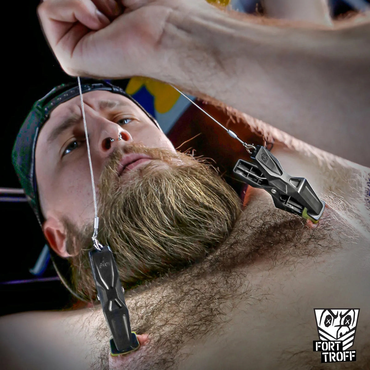 Bearded model on his back while a hand pulls the steel cord of his nipple clamps, Fort Troff gay gear at Boyzshop