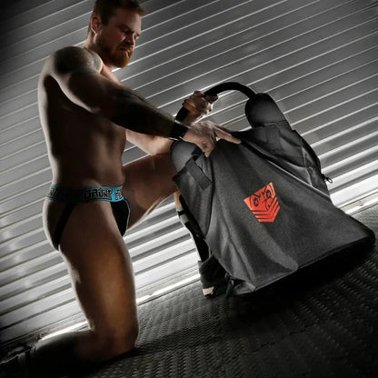 Model kneeling to zip a rim seat into the Rimmer Bag, steel shutter backdrop, Fort Troff gay gear at Boyzshop