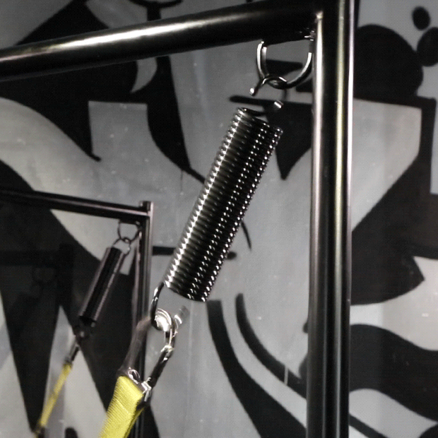 Black sex sling spring hanging from a stand corner with a yellow strap clipped below, Fort Troff gay gear at Boyzshop