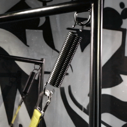 Black sex sling spring hanging from a stand corner with a yellow strap clipped below, Fort Troff gay gear at Boyzshop