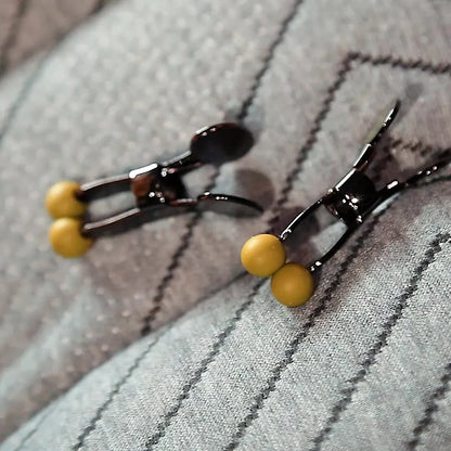 Pair of steel nipple clamps with yellow silicone tips on a gray throw, Fort Troff gay gear at Boyzshop