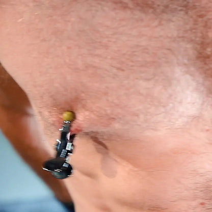 Close-up of a steel nipple clamp locked on, yellow tips holding tight, Fort Troff gay gear at Boyzshop