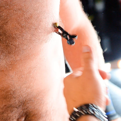 Hand tugging a steel nipple clamp hanging from a hairy chest, Fort Troff gay gear at Boyzshop