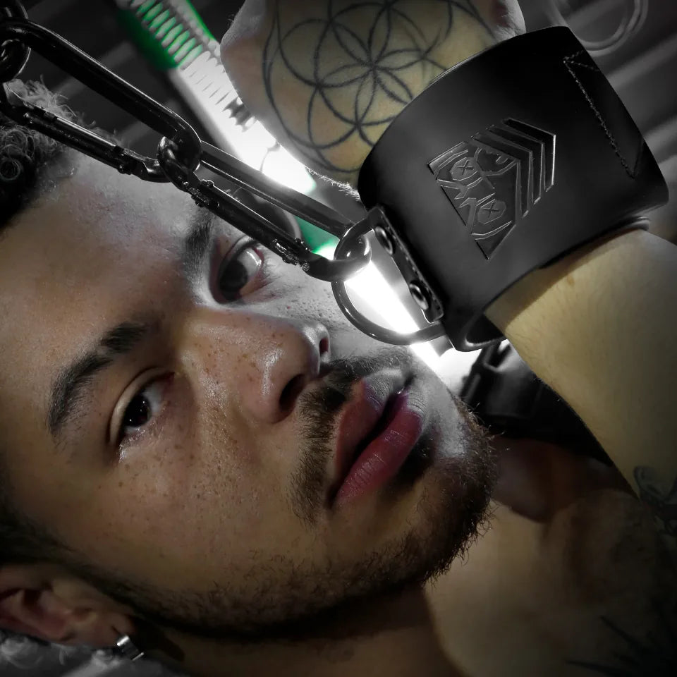 Leather wrist cuff clipped to a steel chain above a model's face, low angle, Fort Troff gay gear at Boyzshop