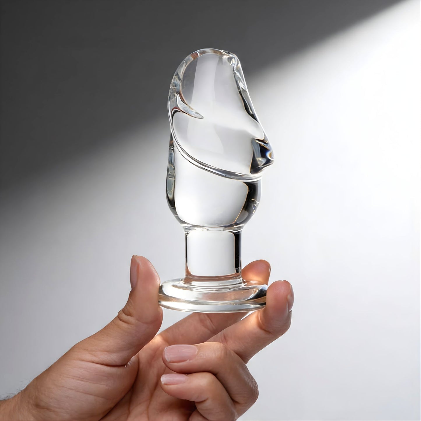 hand holding clear glass butt plug with sculpted cock head tip and flared base