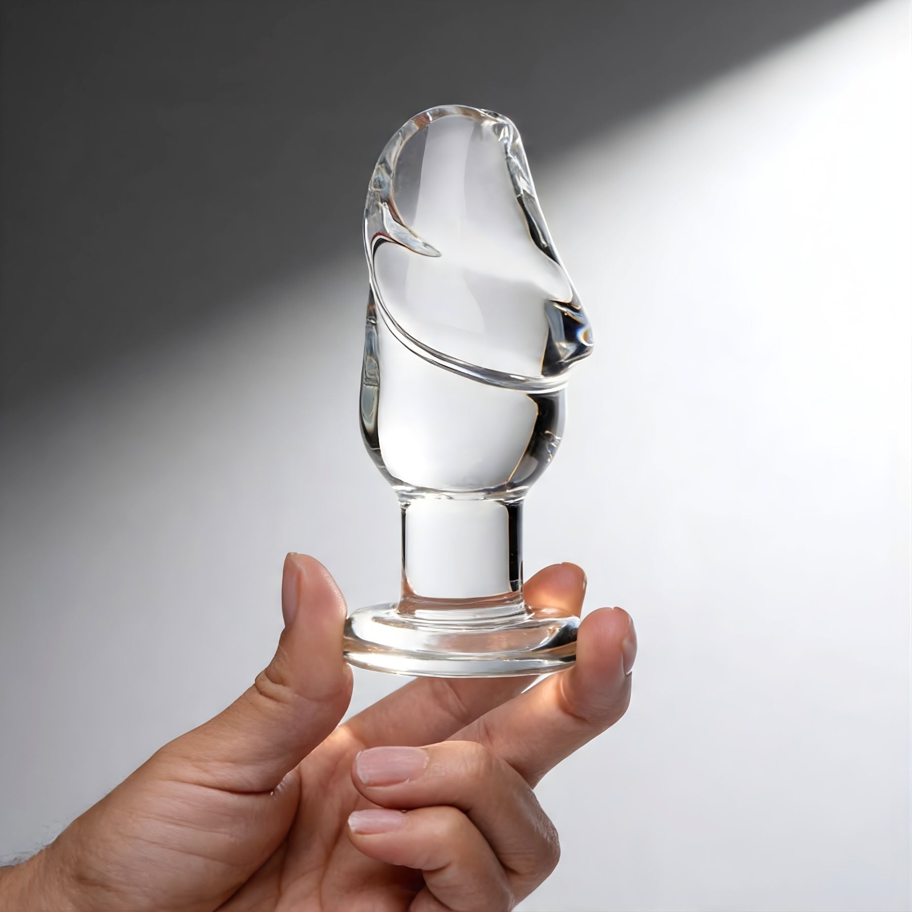 hand holding clear glass butt plug with sculpted cock head tip and flared base