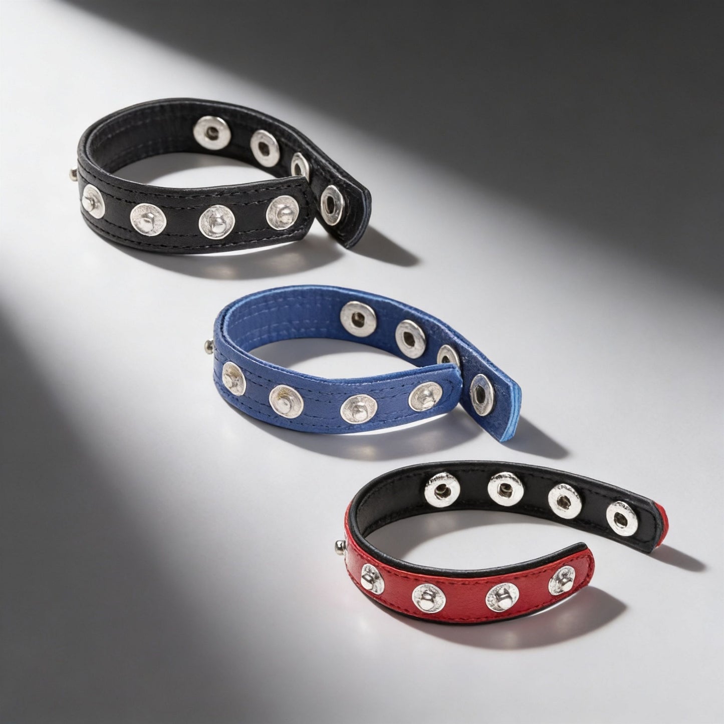 black blue and red leather snap cock rings with silver stud closures displayed on gray background