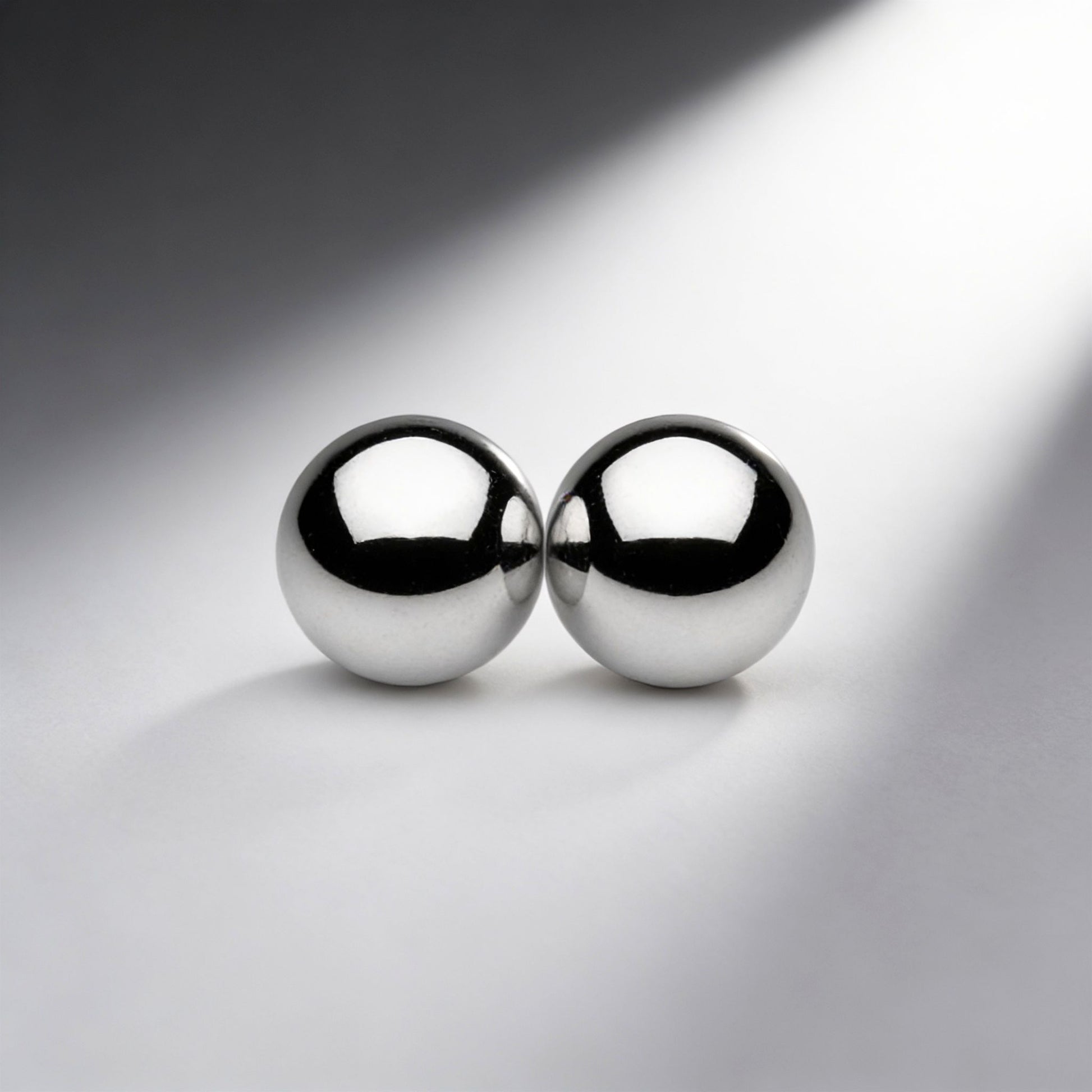 two polished silver magnetic metal orbs touching together on gray background with dramatic lighting