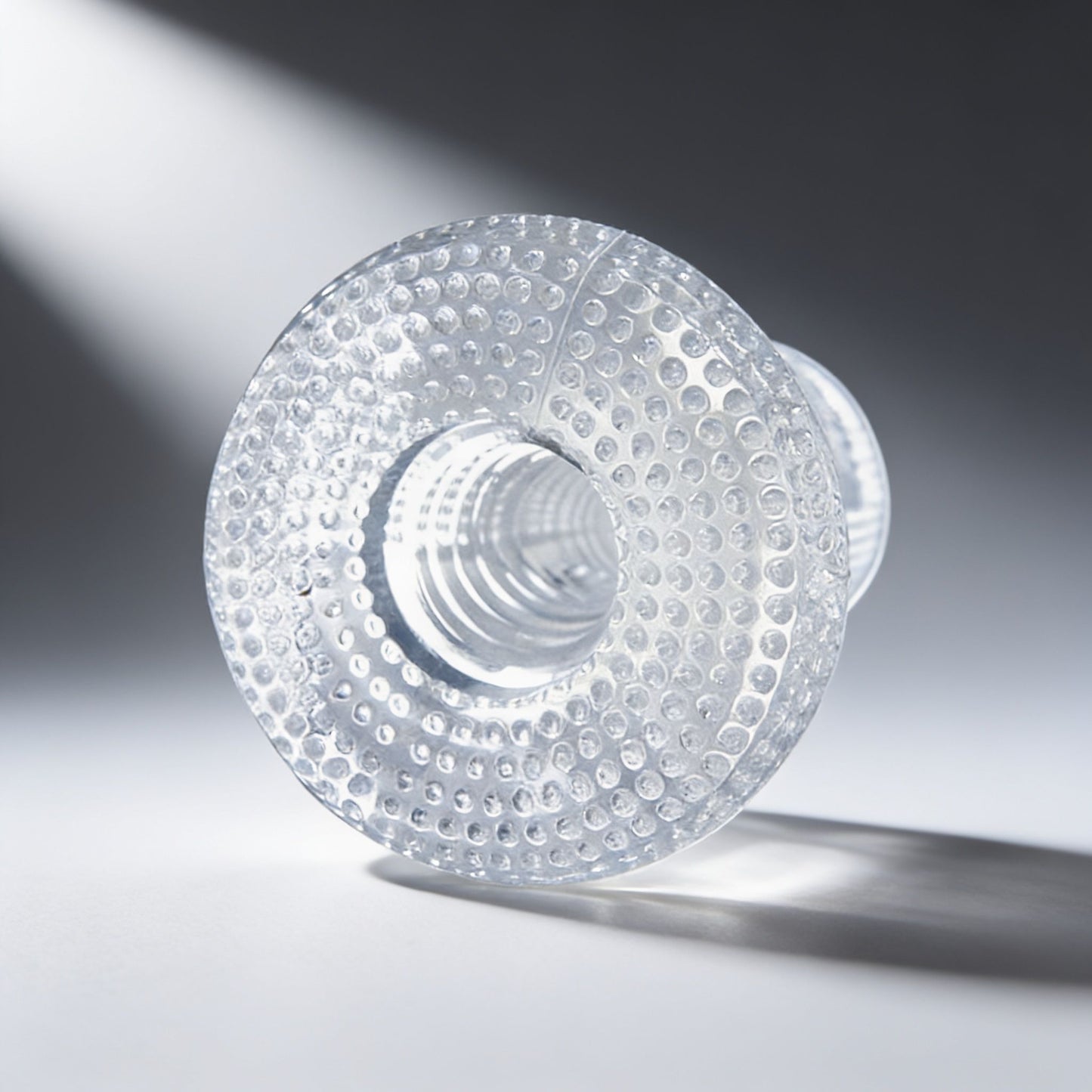 front view of a clear textured male stroker highlighting the entry opening, transparent material, and raised grip texture