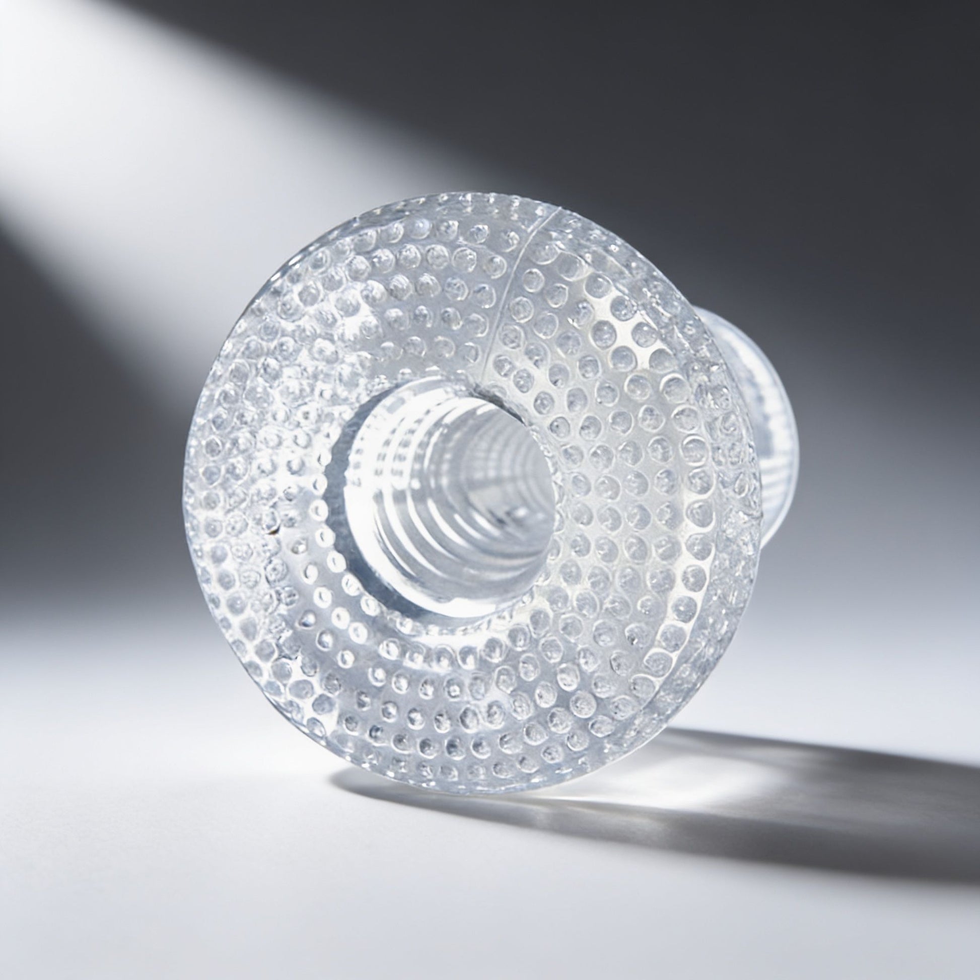 front view of a clear textured male stroker highlighting the entry opening, transparent material, and raised grip texture
