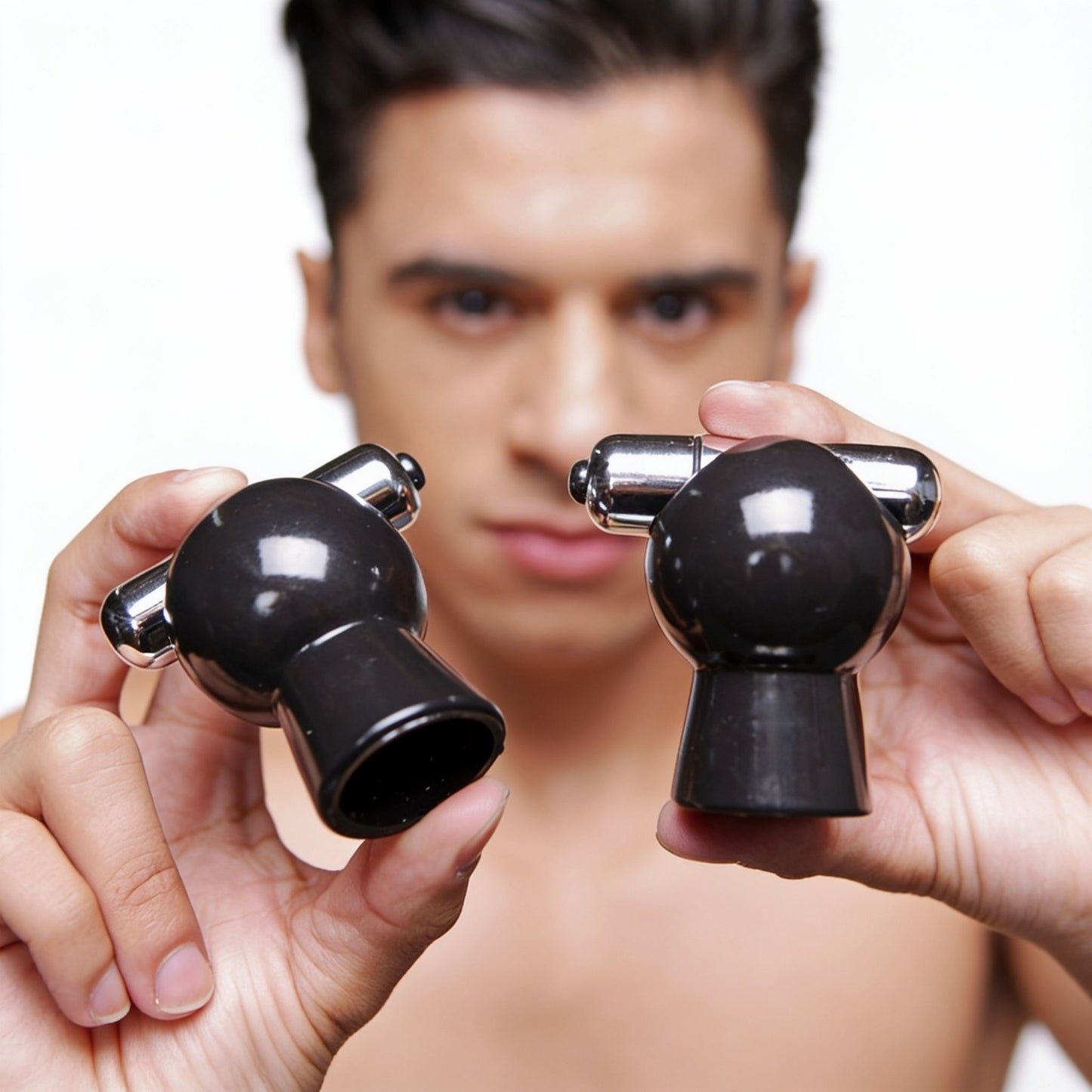 Close-up of a male model holding a pair of black vibrating nipple suckers, highlighting the suction cup openings, integrated bullet vibrators, and smooth ABS construction.
