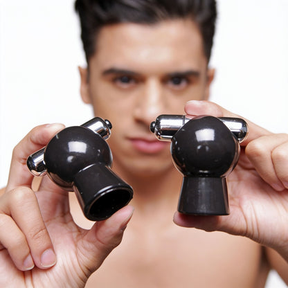 Close-up of a male model holding a pair of black vibrating nipple suckers, highlighting the suction cup openings, integrated bullet vibrators, and smooth ABS construction.