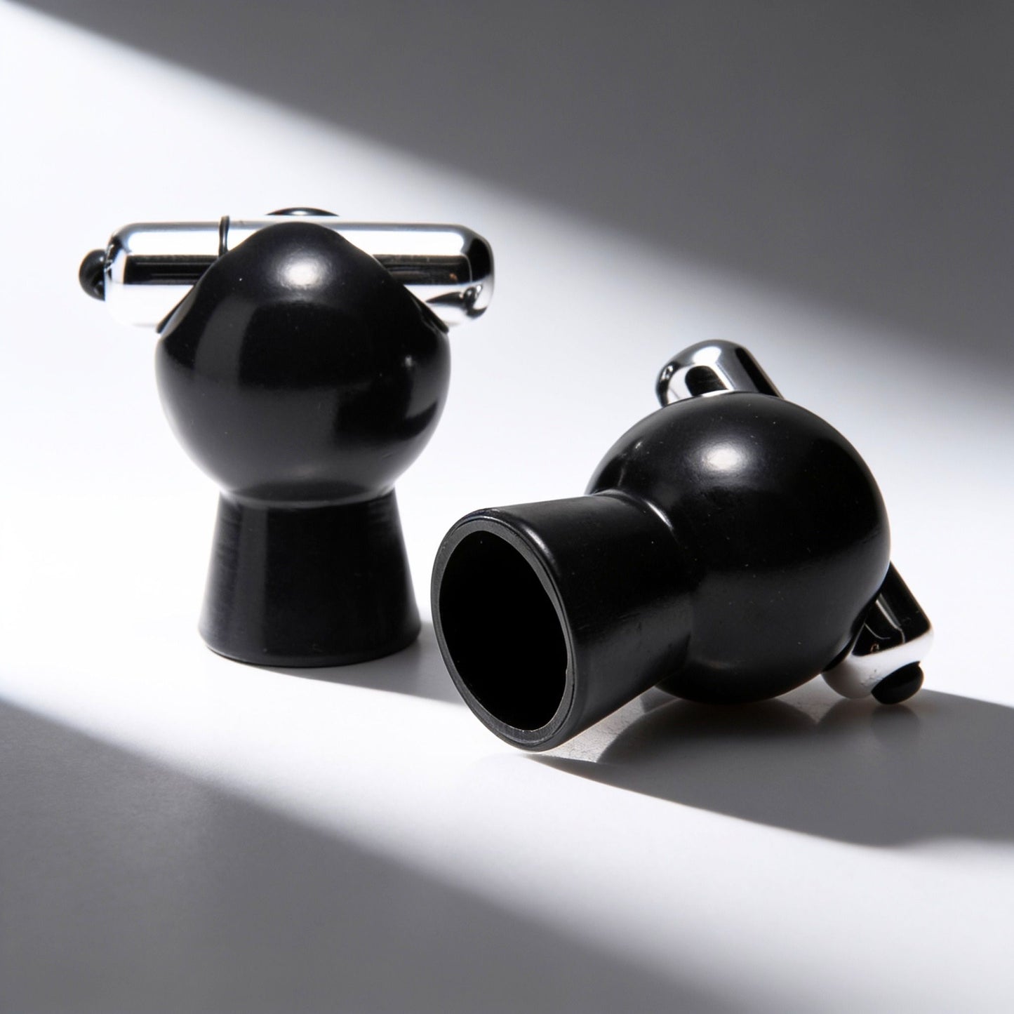 Pair of black vibrating nipple suckers displayed on a white surface, showcasing the vacuum suction cups, removable bullet vibrators, and sleek glossy finish.