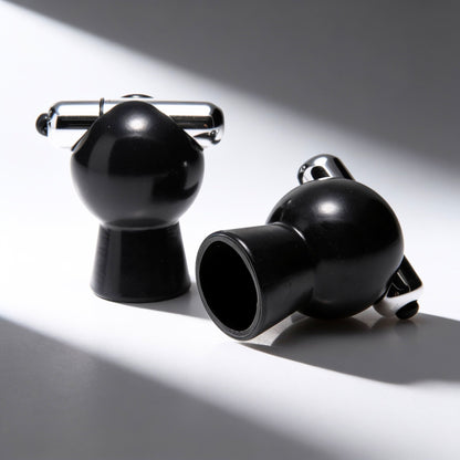 Pair of black vibrating nipple suckers displayed on a white surface, showcasing the vacuum suction cups, removable bullet vibrators, and sleek glossy finish.
