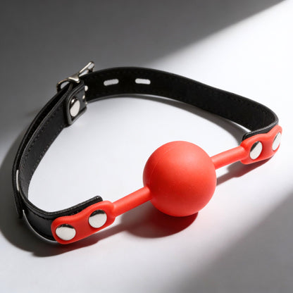 red silicone comfort ball gag with adjustable black strap and silver buckle hardware on gray background