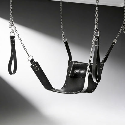 black leather bondage sling with stirrups, chains, and padded pillow suspended against gray background